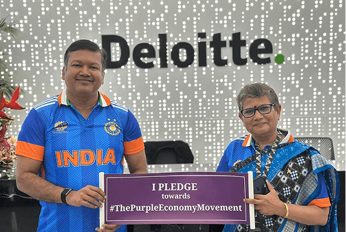 Two individuals in front of a Deloitte office wall holding a sign that reads, "I PLEDGE towards #ThePurpleEconomyMovement."