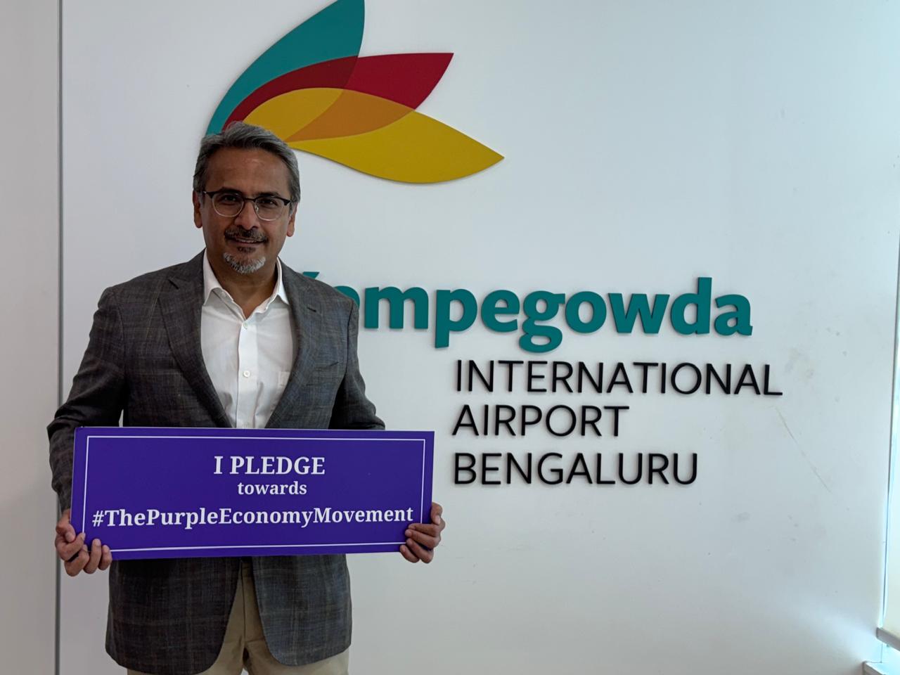 Person holding a Purple Economy pledge sign at Kempegowda Bengaluru International Airport.