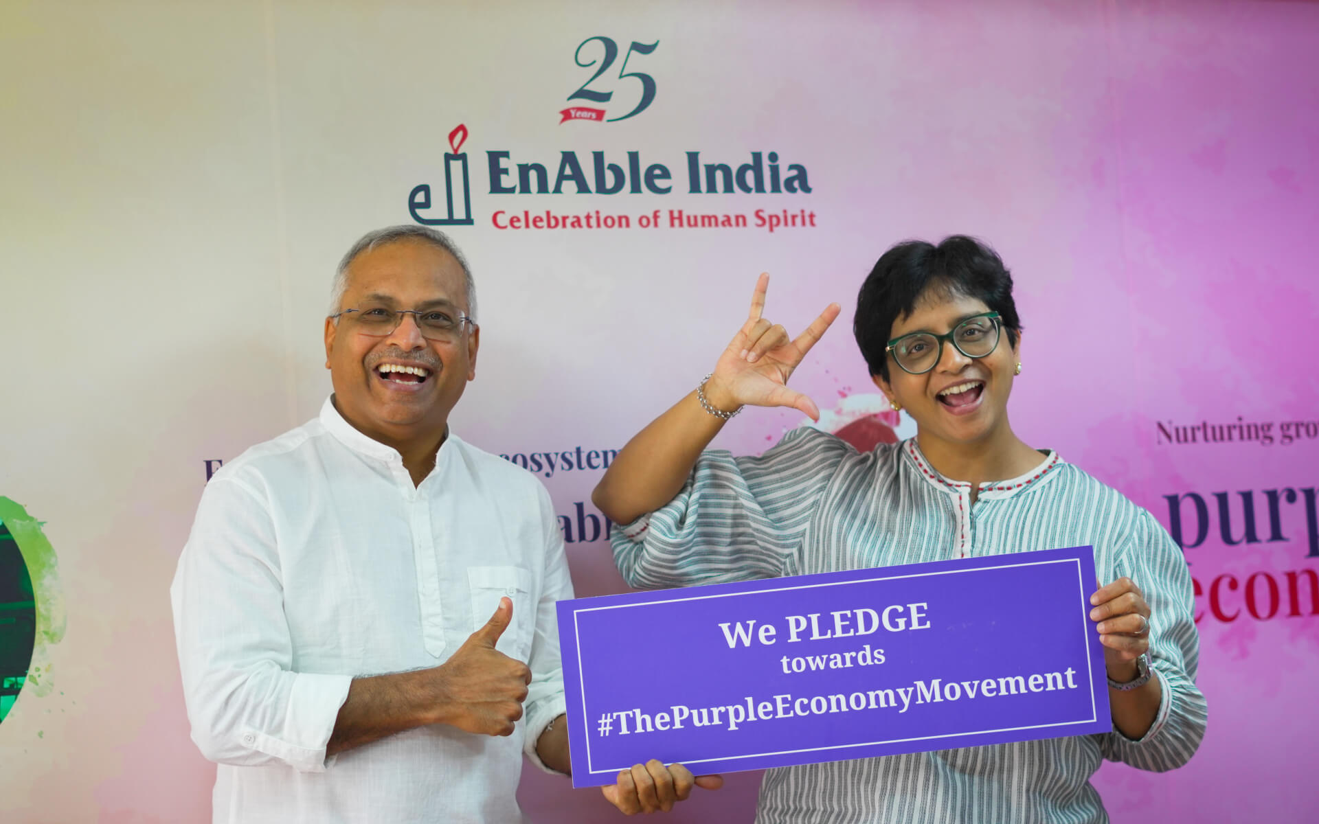 Two people holding a Purple Economy pledge sign at an EnAble India event.