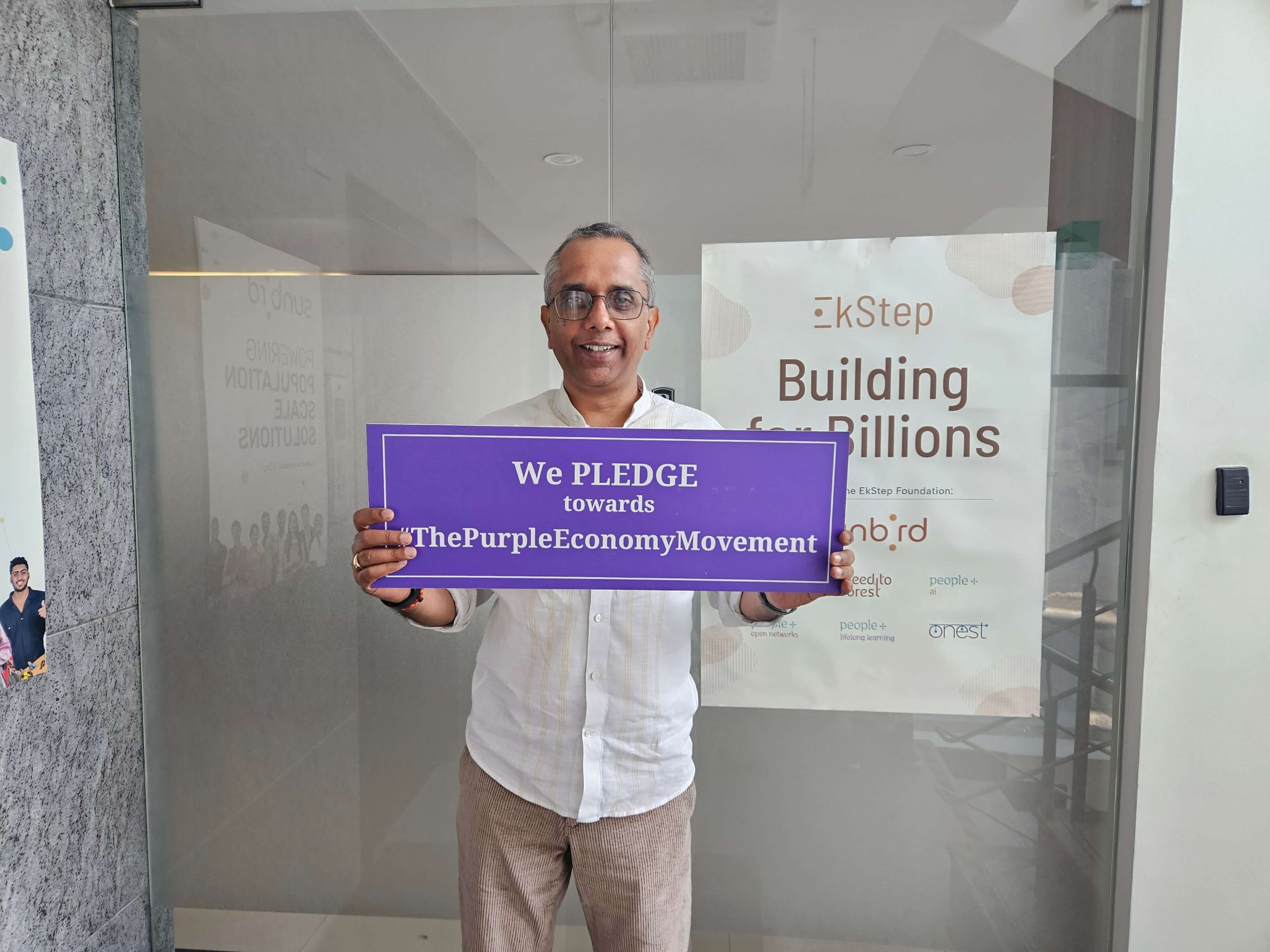 Person holding a Purple Economy pledge sign in front of an EkStep office display.
