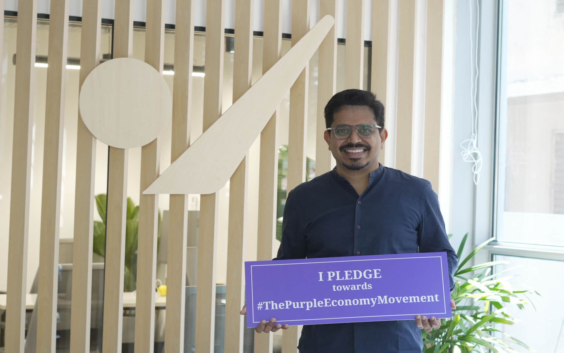Person holding a Purple Economy pledge sign in an Fide office lobby.