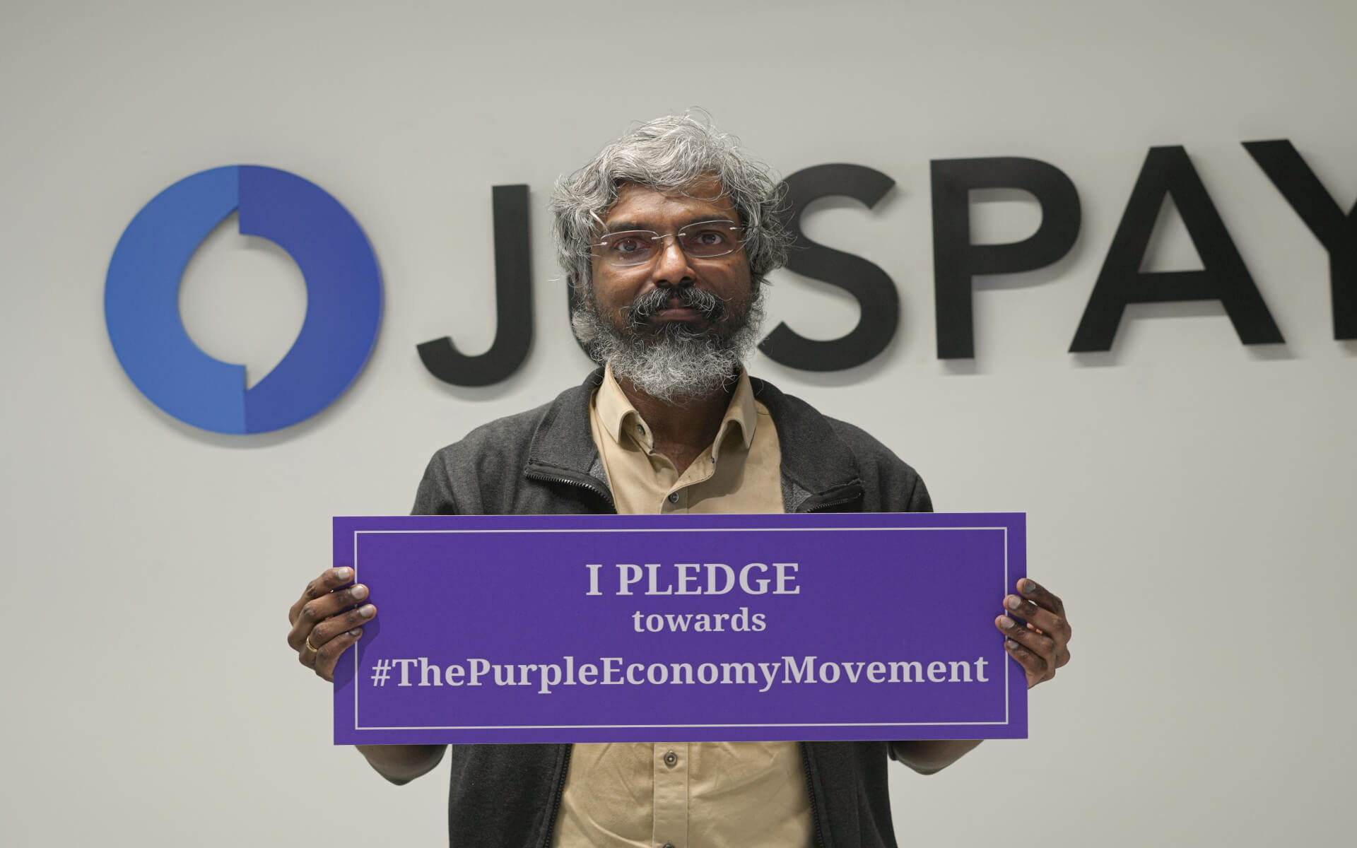 Person holding a Purple Economy pledge sign in an JusPay office lobby.