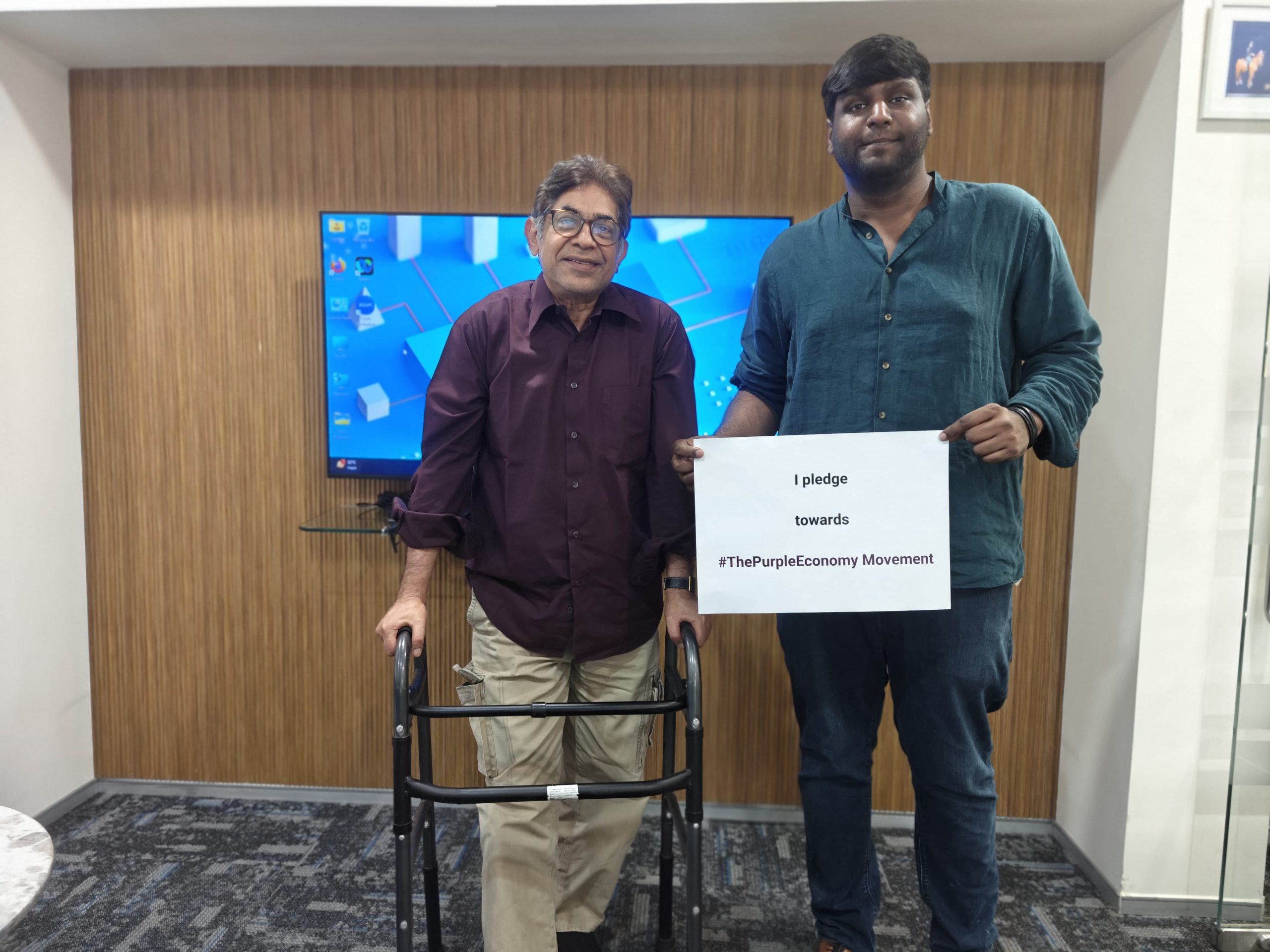 Two people posing with a Purple Economy pledge sign indoors.