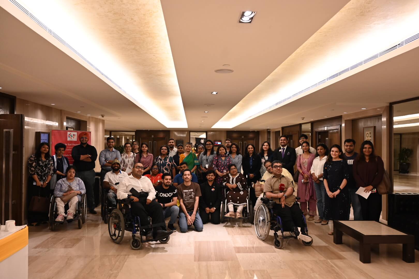 A diverse group of people, including wheelchair users, posing for a photo in a hallway.