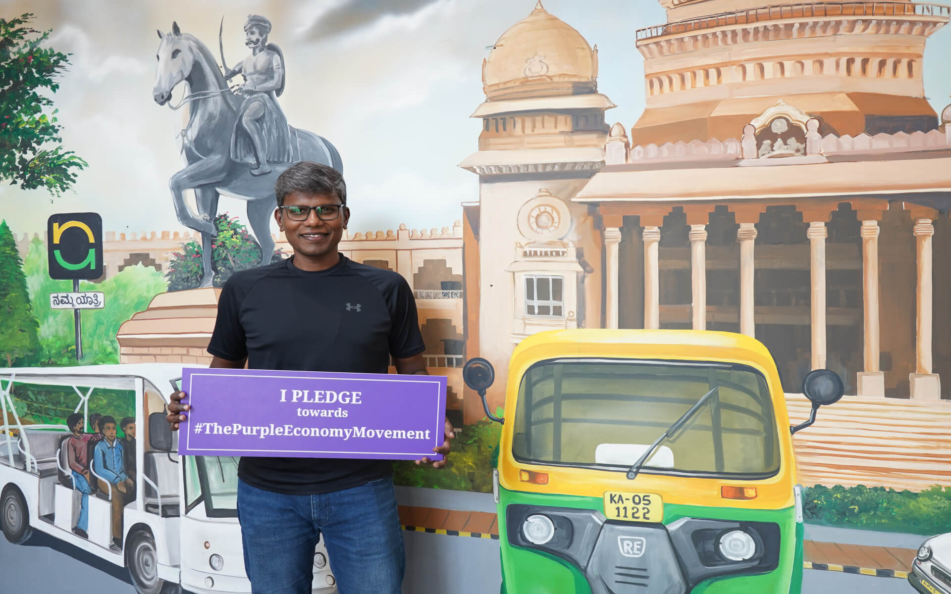 Person holding a Purple Economy pledge sign in front of a Namma Yatri mural.