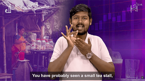 A presenter uses sign language in front of a background showing a small tea stall