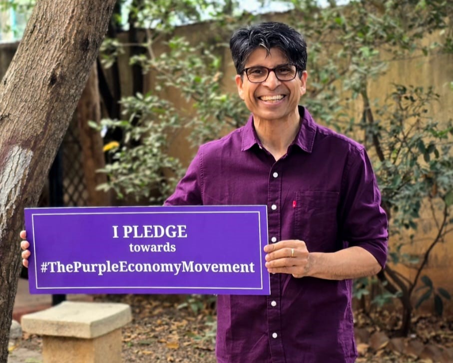 Pramod Varma holding a Purple Economy pledge sign outdoors.