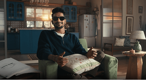 Man wearing sunglasses speaking while seated in a living room.